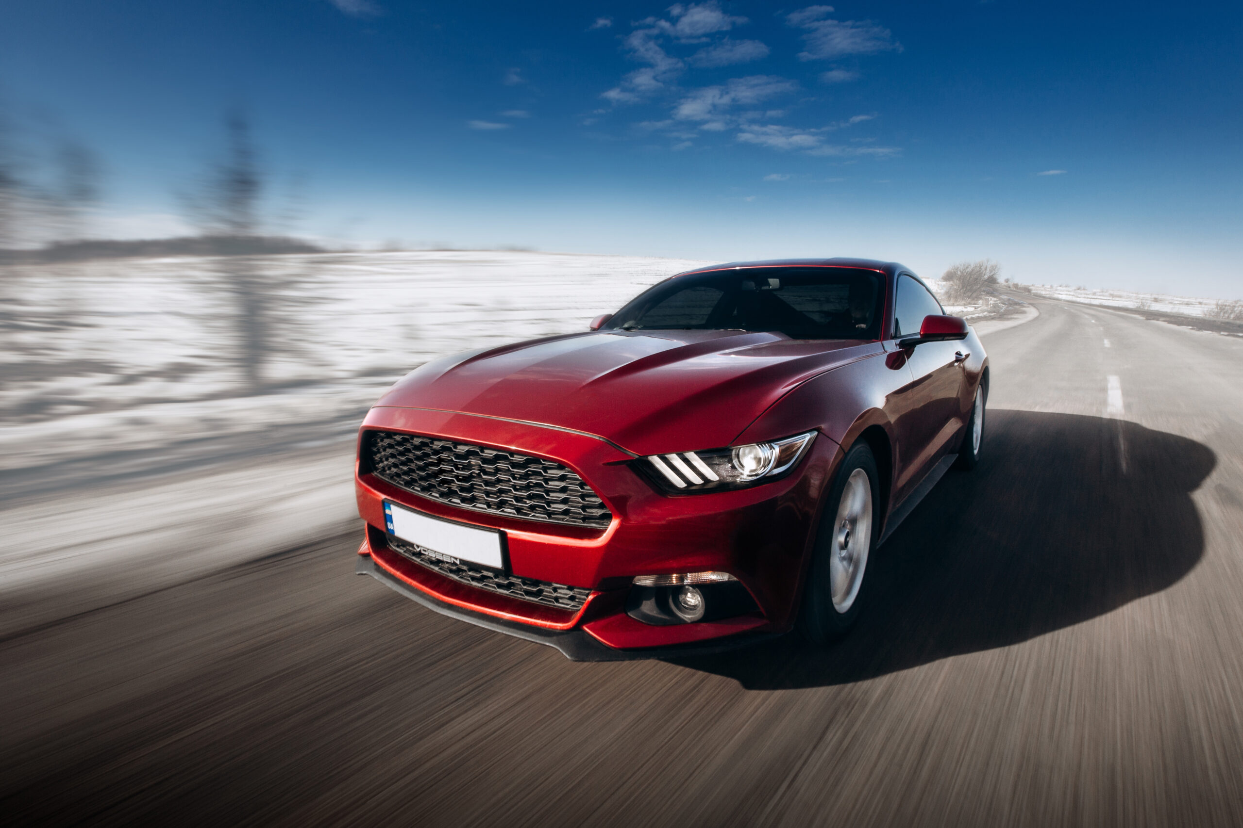 A red 2 door sports car driving down the road. The surroundings are blurry with motion.